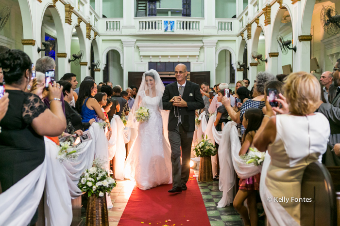 Foto casamento rj noiva entrando com o pai na Igreja nave corredor até altar convidados nos bancos com celular fotografando por kelly fontes fotografia