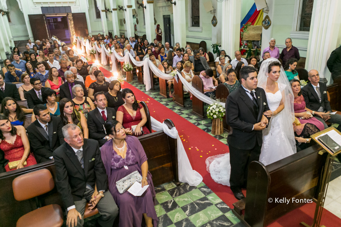 Foto casamento rj noiva e noivo com padre no altar Igreja lotada de convidados e parentes noivos por kelly fontes fotografia