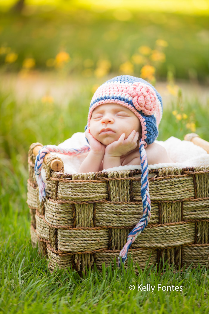 Fotografia Newborn Recém Nascido Bebê com touca azul flor rosa segurando cabeça sobre as mãos dentro cesta RJ por Kelly Fontes